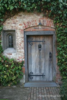 an old door is surrounded by green plants and ivys on the side of a brick building