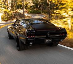 a black car driving down the road with trees in the backgrouund and sunlight shining on it