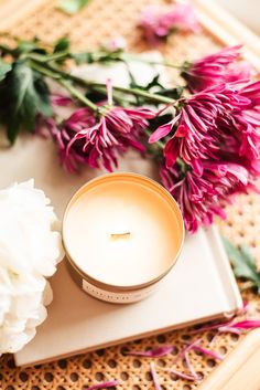 a white candle sitting on top of a wooden tray next to pink and white flowers