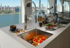 a kitchen sink filled with lots of colorful fruit and veggies next to a window