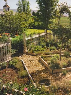 a garden with lots of plants and rocks in it's center, next to a white picket fence