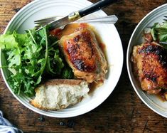 two white bowls filled with meat and vegetables on top of a wooden table next to silverware