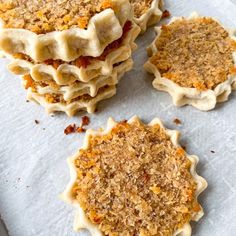 four small pastries are sitting on top of a piece of paper with crumbled toppings