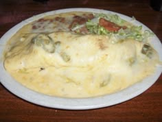 a white plate topped with an omelet covered in cheese and toppings on top of a wooden table