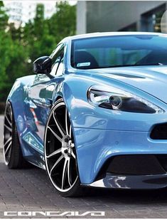 the front end of a blue sports car parked on a brick road with trees in the background