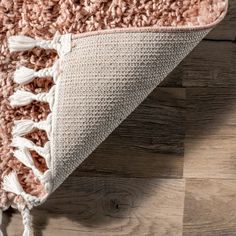 a pink and white rug with tassels laying on top of wooden flooring