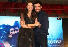 two people standing next to each other in front of a screen with a movie poster behind them