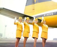 four women in yellow uniforms standing next to an airplane on the tarmac with their hands up