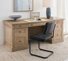 a chair sitting at a desk with a lamp on top of it and a painting hanging above the desk