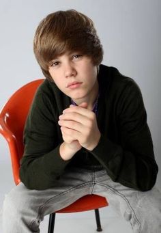 a young man sitting in a chair with his hands folded over his chest and looking at the camera