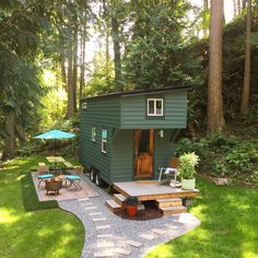 a tiny green house in the middle of a forest with picnic tables and chairs around it