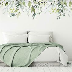 a white bed sitting under a green leafy wall mural