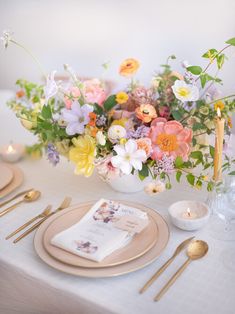 an arrangement of flowers in a vase on a white table cloth with gold cutlery