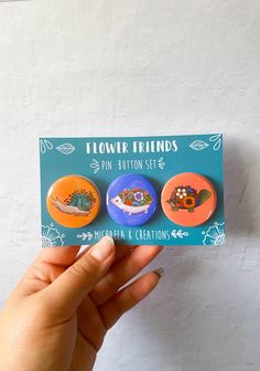 someone is holding up some buttons for their friend's button set, which includes three different designs