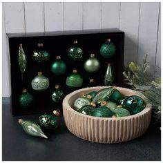 a bowl filled with green christmas ornaments next to a black box