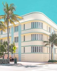 a large white building with palm trees in front of it and a street sign on the corner