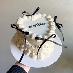 a hand holding a white cake with black ribbon around it and the word nineteen on top