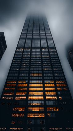 the top of a tall building lit up at night with fog and low clouds in the sky