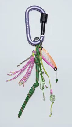 a green and pink fish hanging from a hook on a white background with an object in the foreground