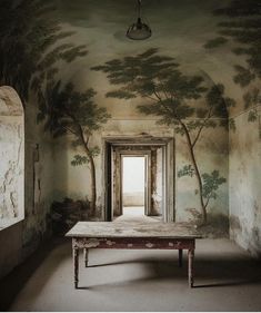 an empty room with trees painted on the walls and a table in front of it