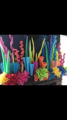 there are many different colored objects on the wall in front of the window, and one is made out of plastic straws