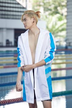 a person standing in front of a swimming pool wearing a white and blue jacket with an open back