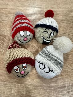 three knitted balls with faces on them sitting on a wooden surface, one is wearing a hat and the other has a pom