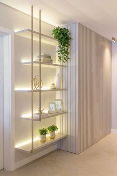 a white shelf with plants and pictures on it in front of a wall that has vertical slats