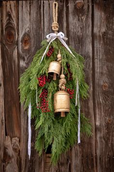 a christmas wreath with bells hanging from it's side on a wooden wall next to a fence