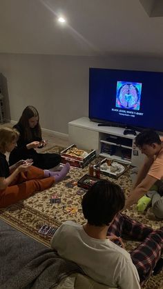 four people sitting on the floor in front of a tv