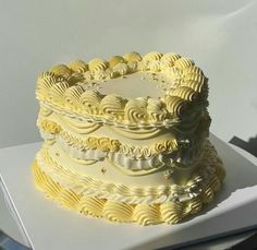 a white and yellow cake sitting on top of a table next to a laptop computer