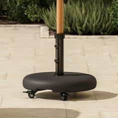 an umbrella stands on wheels in front of a planter and shrubbery, while the sun shines through