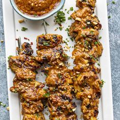 grilled chicken skewers on a platter with a bowl of sauce