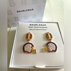 a pair of earrings with football and helmet on them in a white box next to a sign