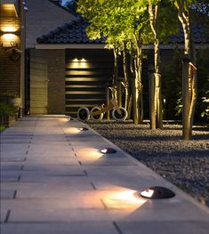 an outdoor walkway lit up with lights and some bikes parked in the driveway next to it