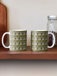 two coffee mugs sitting next to each other on a wooden shelf near a mason jar