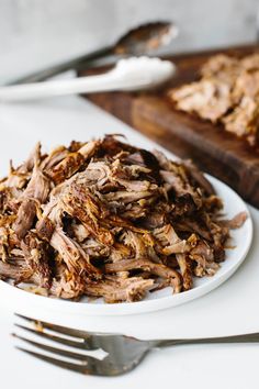 a white plate topped with shredded meat next to a knife and fork on a table