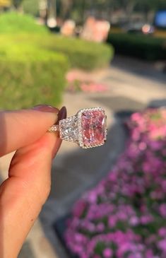 someone is holding an engagement ring with a pink diamond in the middle and purple flowers behind it