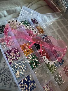 a plastic container filled with lots of different types of sequins next to a pink ribbon