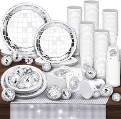 a table topped with lots of shiny plates and silver cups filled with disco ball decorations