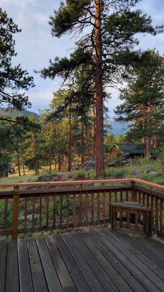 a wooden deck with a bench next to a tall tree in the distance and mountains in the background