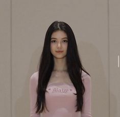 a woman with long black hair standing in front of a wall wearing a pink bodysuit