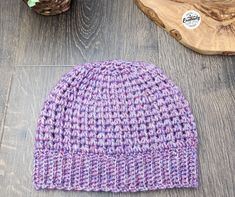 a purple knitted hat sitting on top of a wooden table next to a potted plant