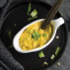 a black plate with a white spoon filled with yellow sauce and garnished with cilantro