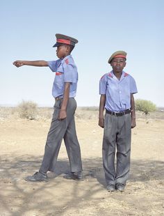 two young boys in uniforms pointing at something off to the side on a dirt field