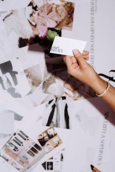 a person holding up a white business card in front of many photos and letters on the wall