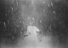 a black and white photo of rain falling down on a bird in the dark sky