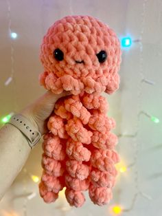 a pink crocheted octopus stuffed animal hanging from a string with lights in the background