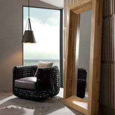 a living room with a chair, mirror and large window looking out to the ocean