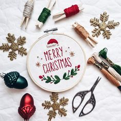 a cross - stitch christmas ornament surrounded by sewing needles and other crafting supplies